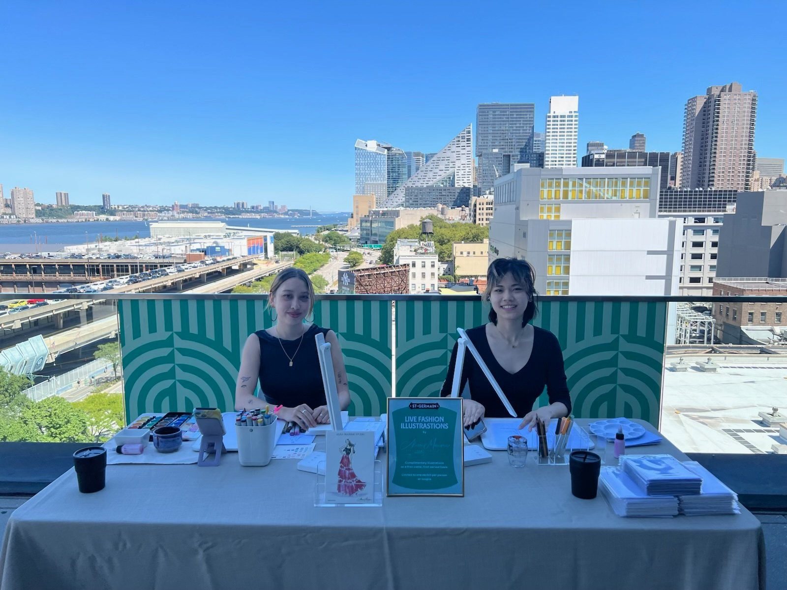 Two artists set up under an umbrella at a rooftop brand activation
