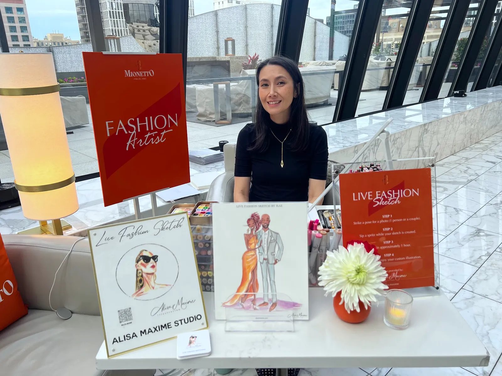 An artist set up at an office event, the city behind the windows